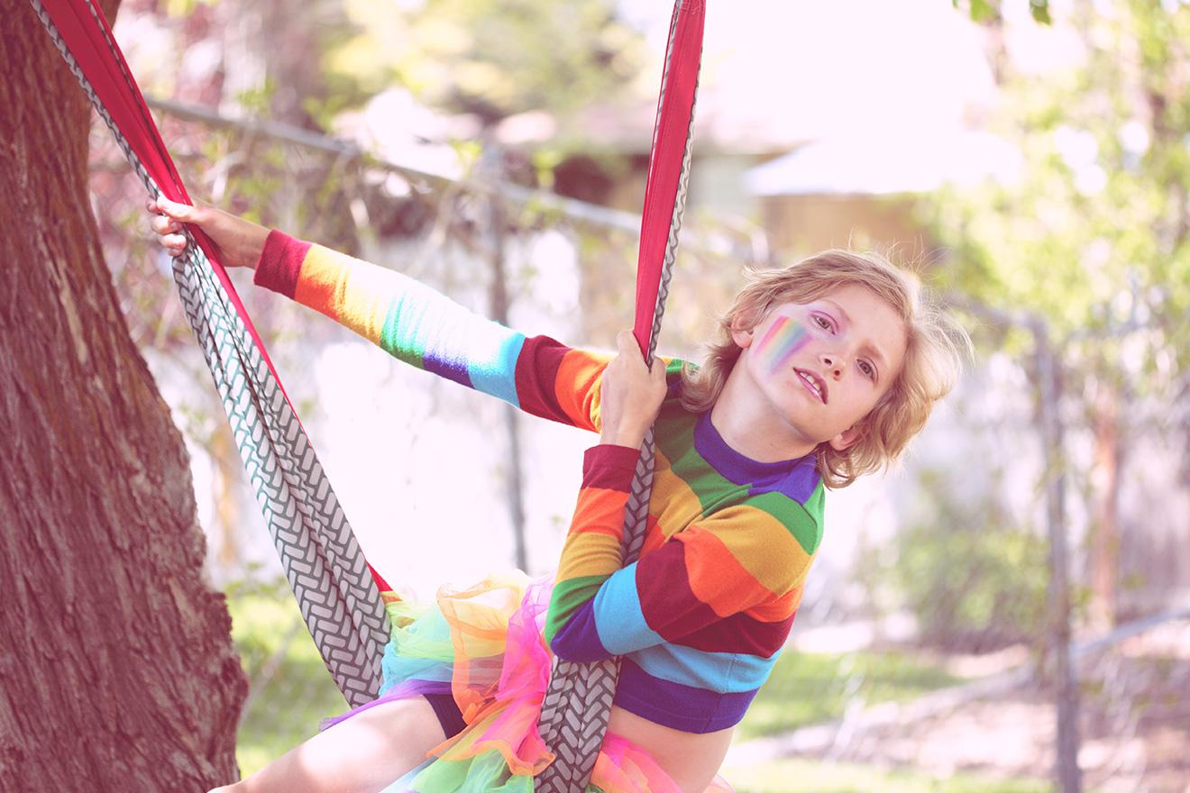 Child on a swing wearing a rainbow-striped shirt and tutu